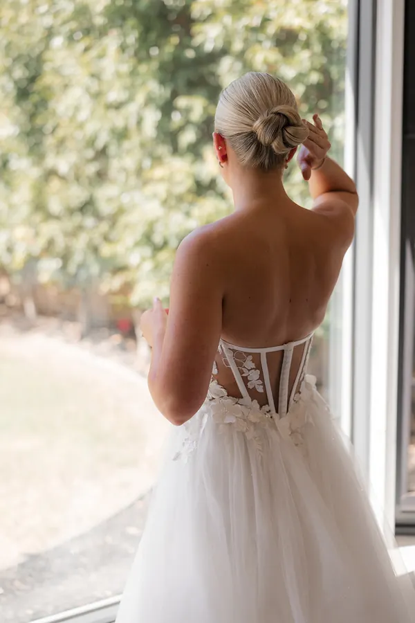 Seen from behind at a window, blonde hair twisted into a low knot