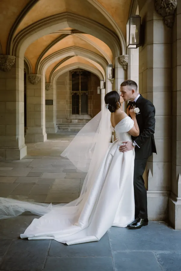 Bride and groom under stone arches, hair in a low bun beneath a cathedral veil