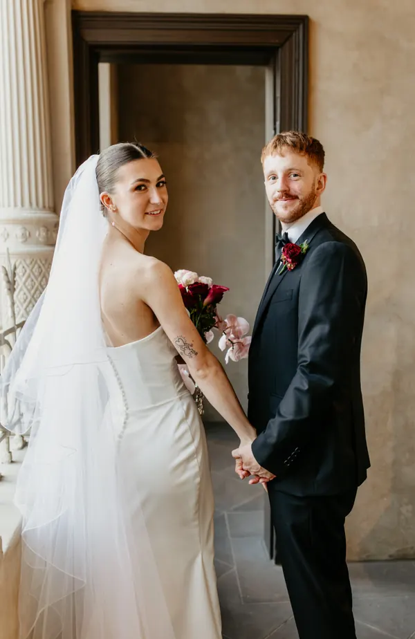 Bride and groom looking back over their shoulders, hair pulled back beneath a long veil