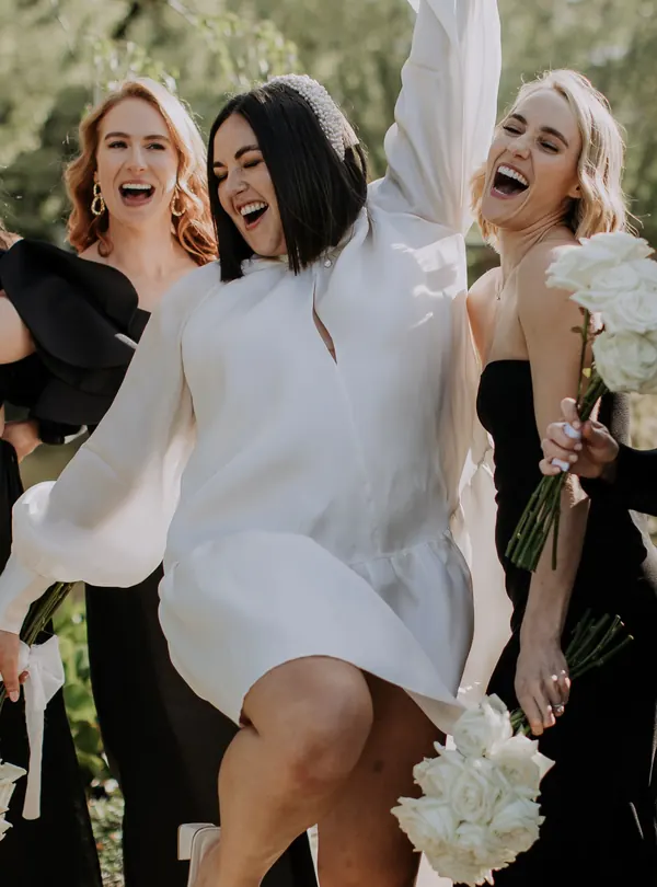 Laughing with her bridesmaids in the sun, dark hair in a sharp bob