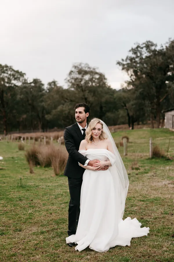 A couple in an open field at dusk, blonde waves under a soft veil