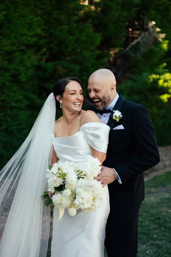Bride and groom laughing in the garden, hair pinned back beneath a long veil