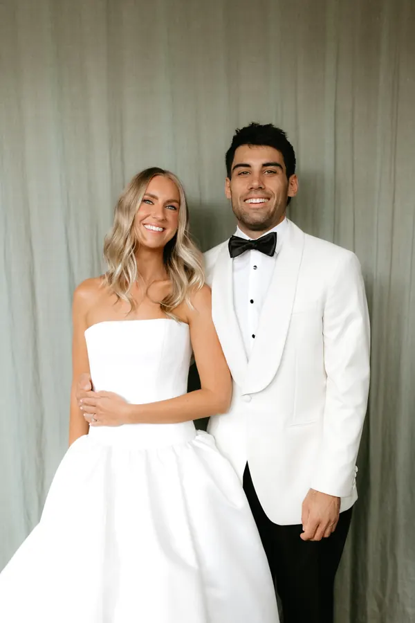 Bride and groom against a soft curtain, blonde hair in loose waves