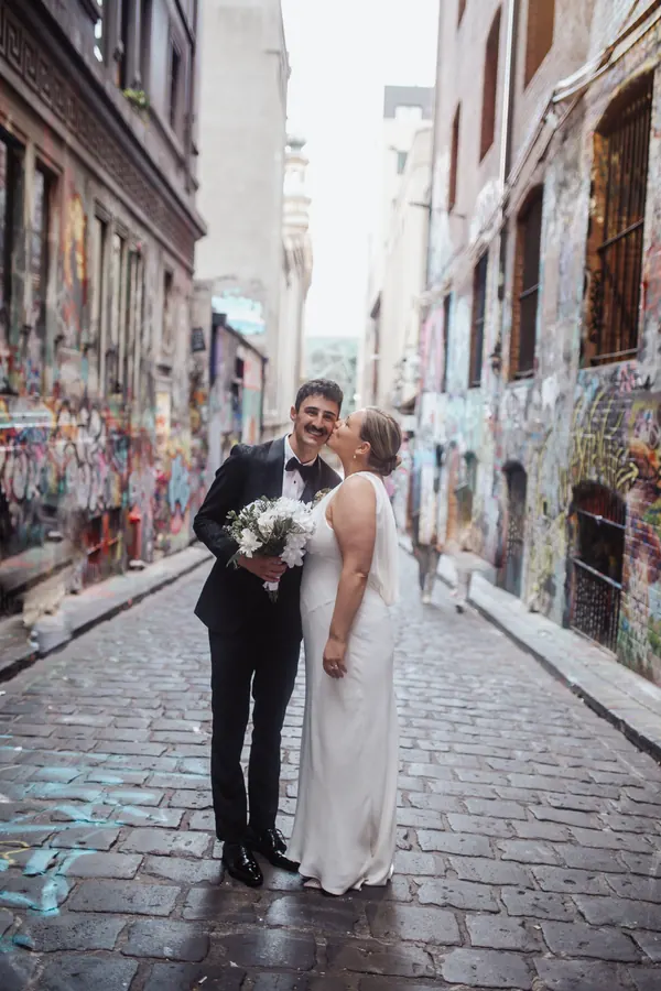 A kiss in a graffitied laneway, hair gathered into a low twist