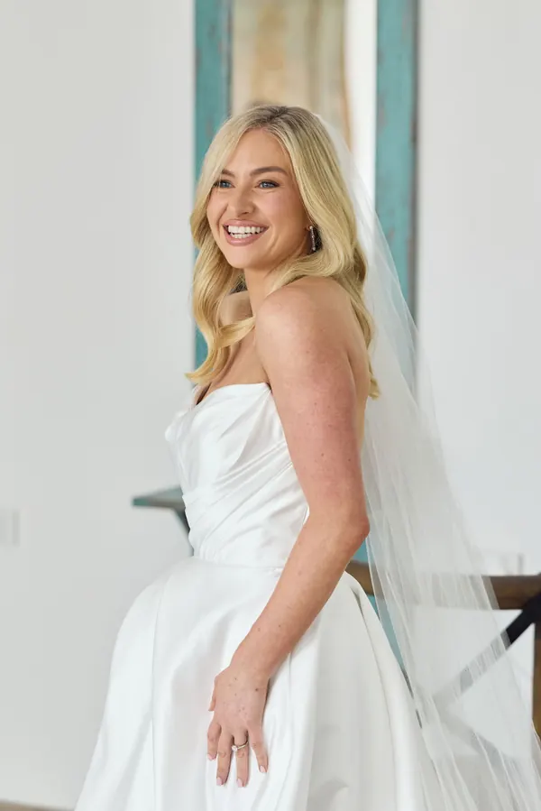 Bride laughing in a strapless gown, blonde hair worn long beneath a veil