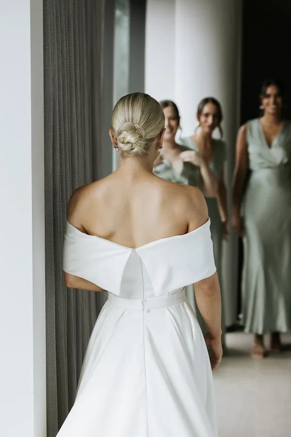 Seen from behind in a doorway, blonde hair twisted into a low knot