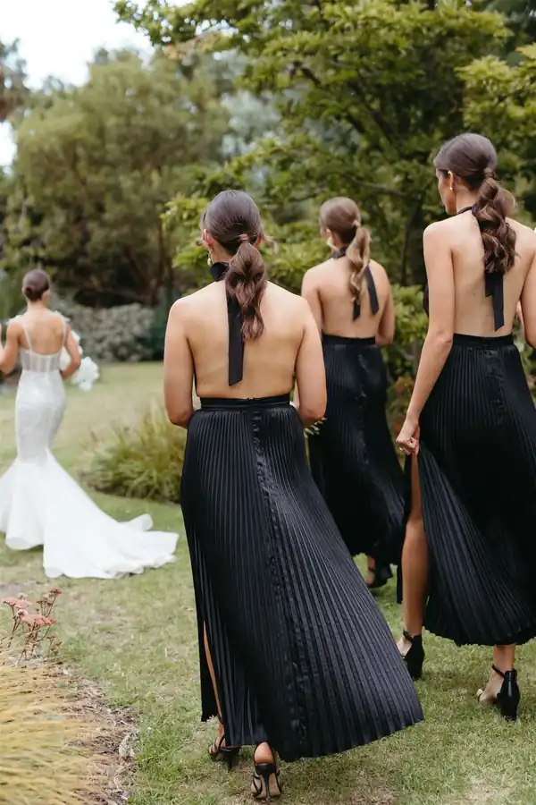 The bride and her party walking away through a garden, hair in long braids