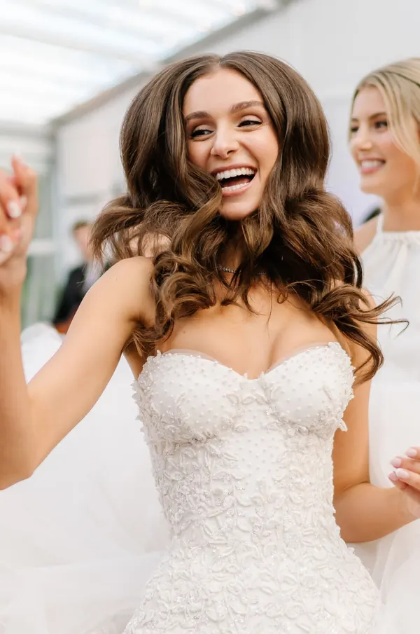 Bride laughing with her arms lifted, long brown curls over a beaded gown
