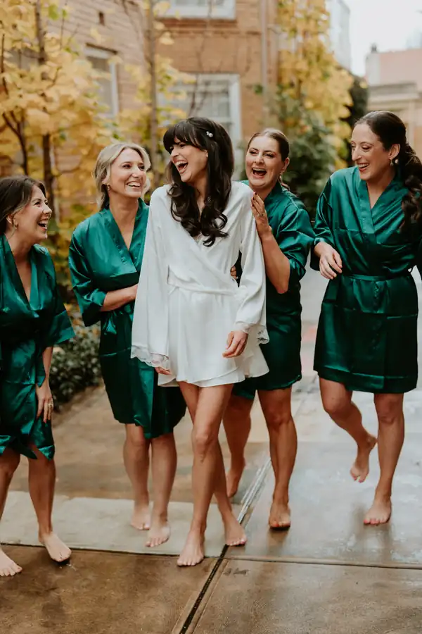 The bridal party laughing barefoot in a courtyard, hair already done