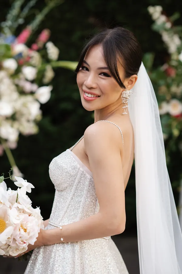 Under blossom with a bouquet, hair swept back beneath a veil
